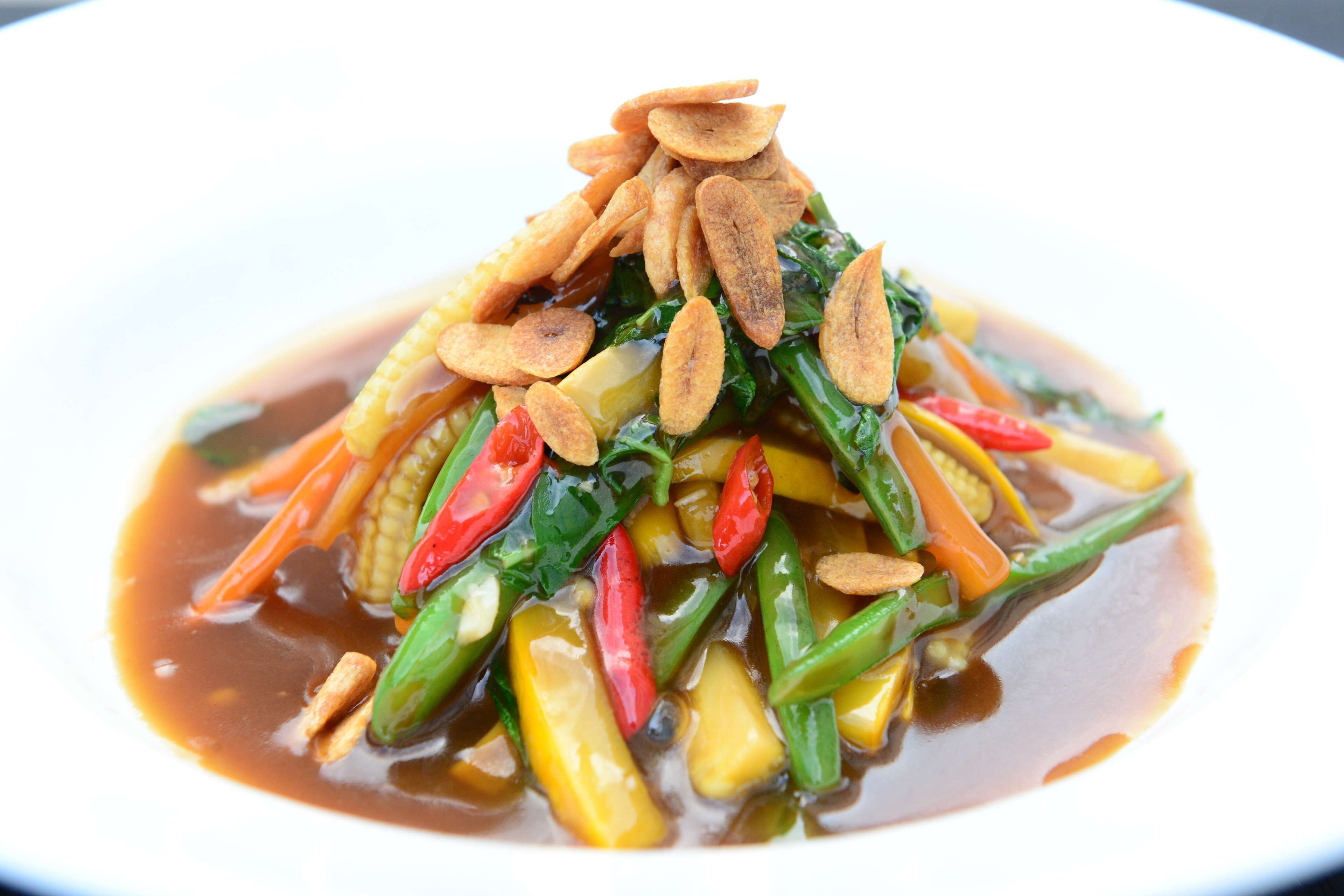 A dish of stir-fried vegetables with a clear sauce, topped with fried shallots.