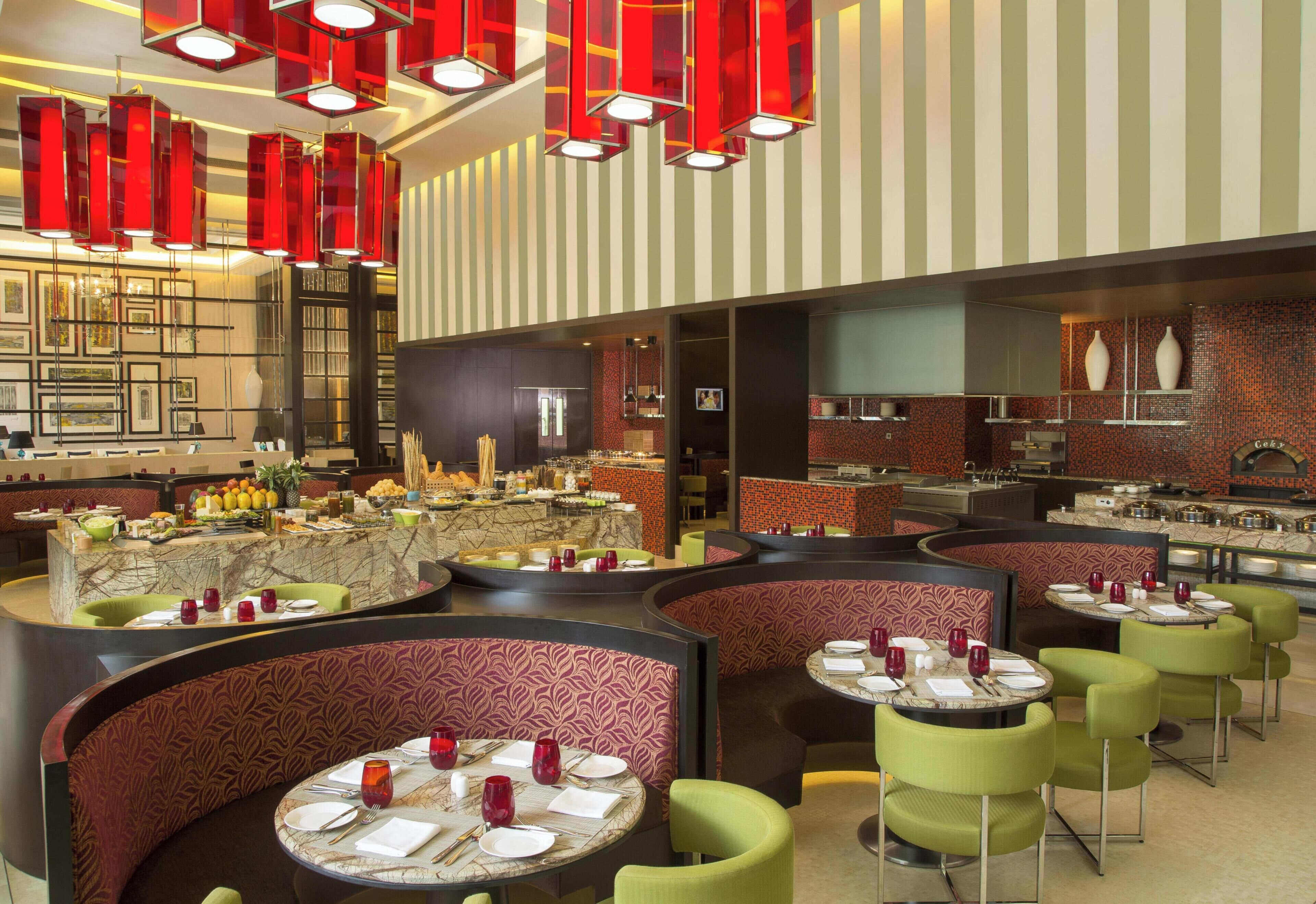 A restaurant with round tables, green chairs, and red pendant lights.