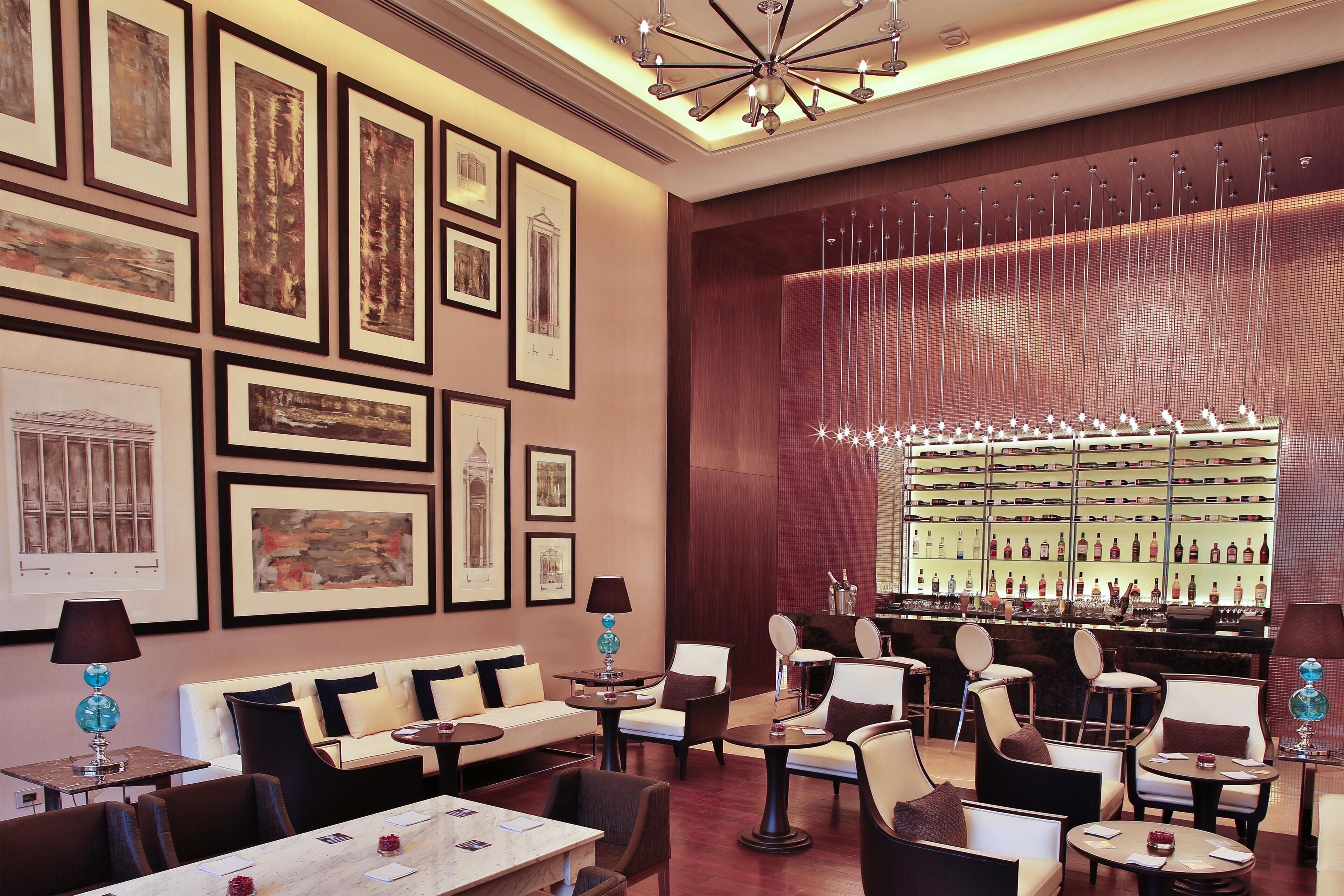 A hotel lobby with framed artwork on the walls, a bar area with a wine display, and seating arrangements.