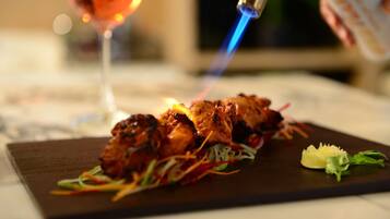 A charred meat dish on a dark plate with a glass of red wine and a can of sauce in the background.
