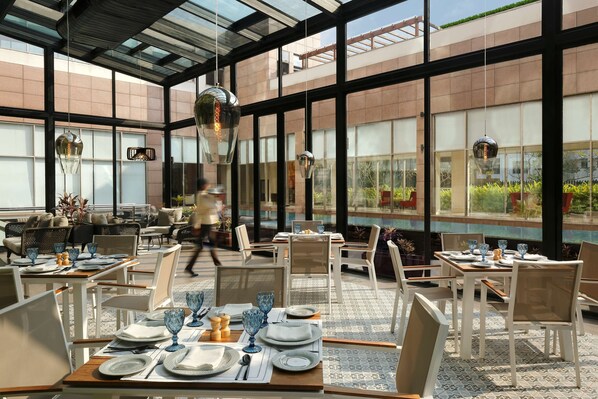 Un restaurante moderno con paredes de vidrio, mesas ordenadas y lámparas colgantes.