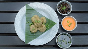 Un plato de dumplings sobre un plato blanco, acompañado de una hoja y tres recipientes pequeños con salsas para mojar.