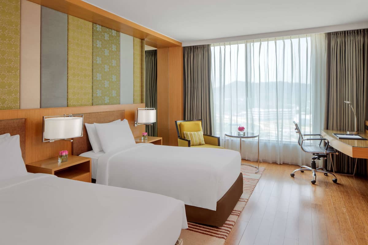 Ein Hotelzimmer mit zwei Betten, einem Schreibtisch, einem Sessel und Blick auf die Stadt.