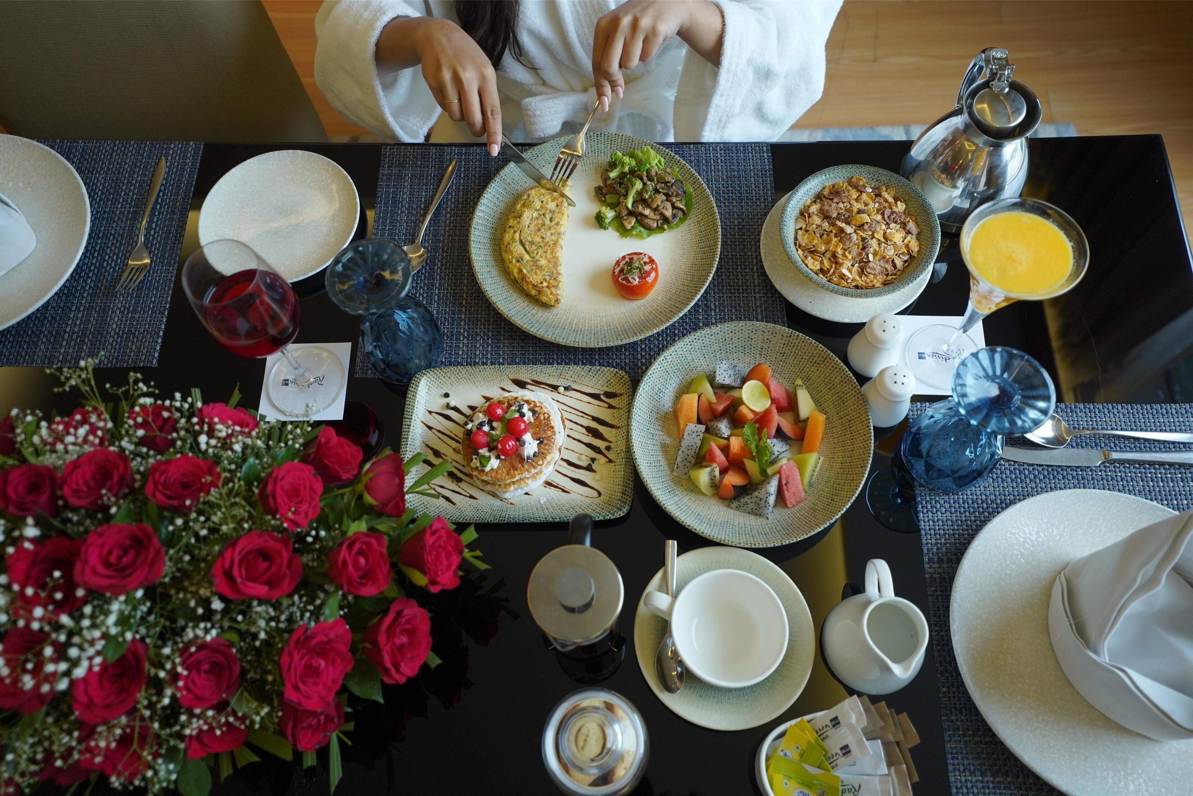 A breakfast setting with plates of food, a coffee pot, a pitcher, and a vase of red roses.