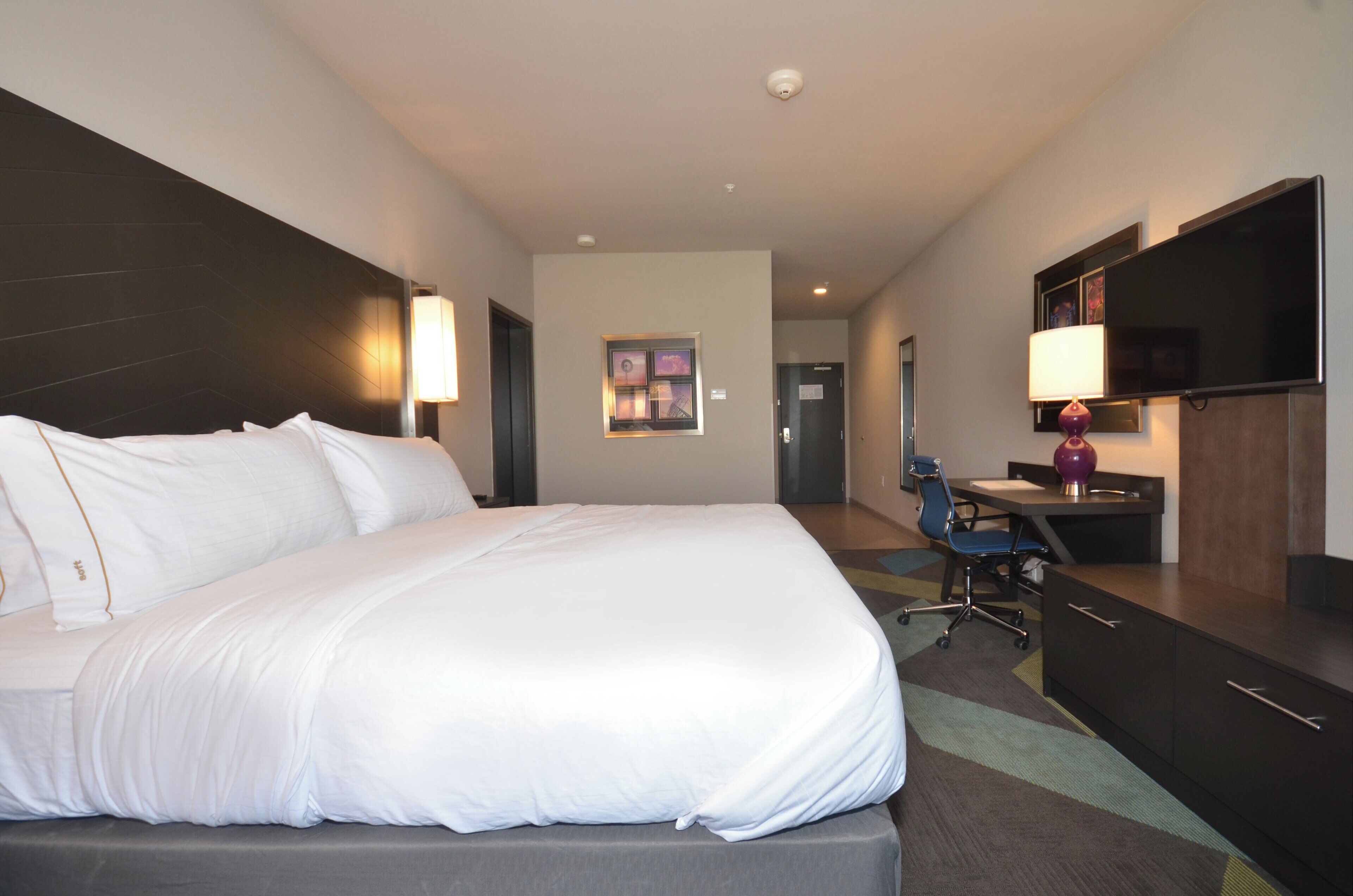 Habitación de hotel con una cama grande, un escritorio, una silla, un televisor y una puerta.