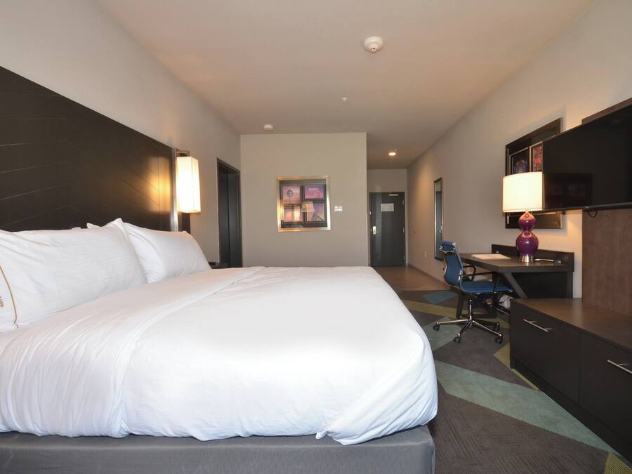 Habitación de hotel con una cama grande, un escritorio, una silla, un televisor y una puerta.