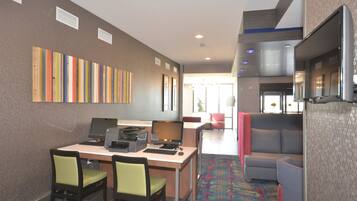 A hotel room with a desk, chairs, a couch, and a colorful wall art piece.