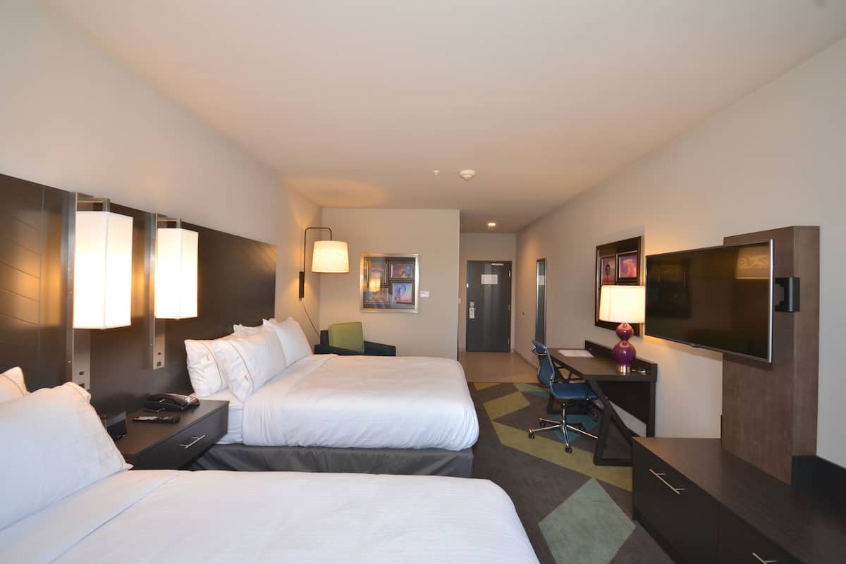 A hotel room with two beds, a desk with a chair, a television, and a door leading to a bathroom.