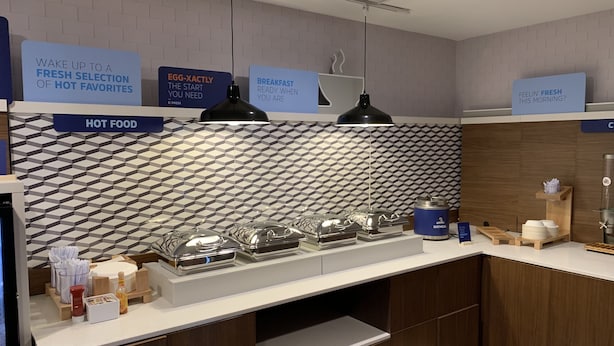 Una barra de desayuno moderna con un salpicadero geométrico, carteles indicando comida caliente y desayuno, y una variedad de productos para el desayuno.