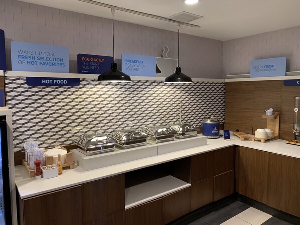 A modern breakfast bar with a geometric backsplash, labeled signs for hot food and breakfast, and a variety of breakfast items.