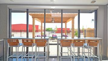 Ein moderner Innenbereich mit Sitzgelegenheiten, großen Fenstern, einer Holzpergola und Blick auf ein rotes Gebäude.