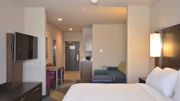 A hotel room with a bed, a desk, a chair, a television, and a kitchenette.