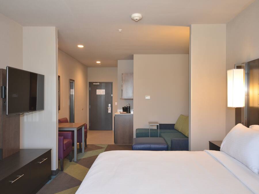 A hotel room with a bed, a desk, a chair, a television, and a kitchenette.