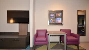 A hotel room with a flat-screen TV, a small table, two chairs, and a wall-mounted artwork.