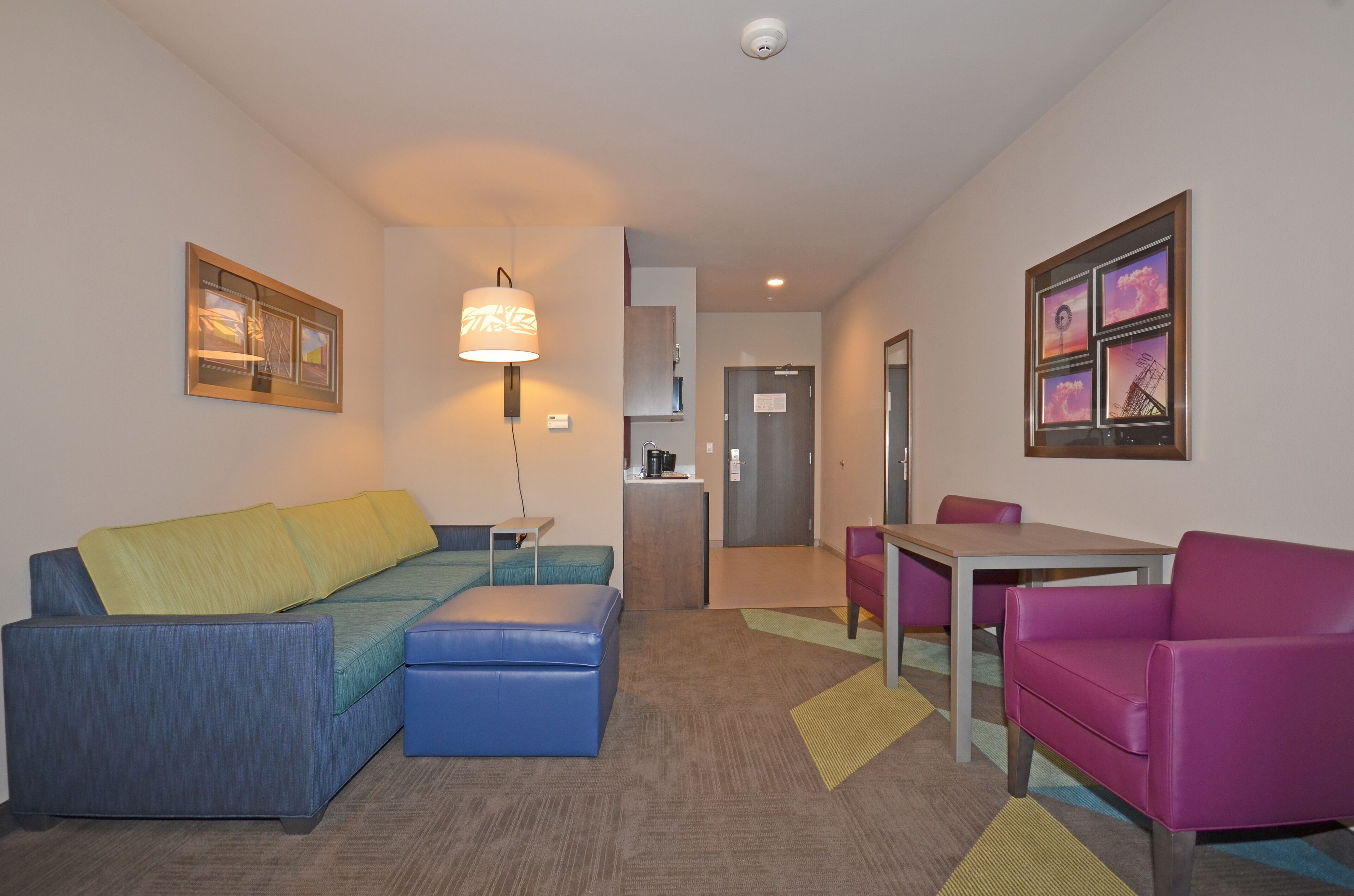 A modern hotel room with a sofa, ottoman, and a small table with chairs.