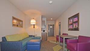 Una habitación de hotel moderna con sofá, reposapiés y una pequeña mesa con sillas.