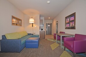 A modern hotel room with a sofa, ottoman, and a small table with chairs.