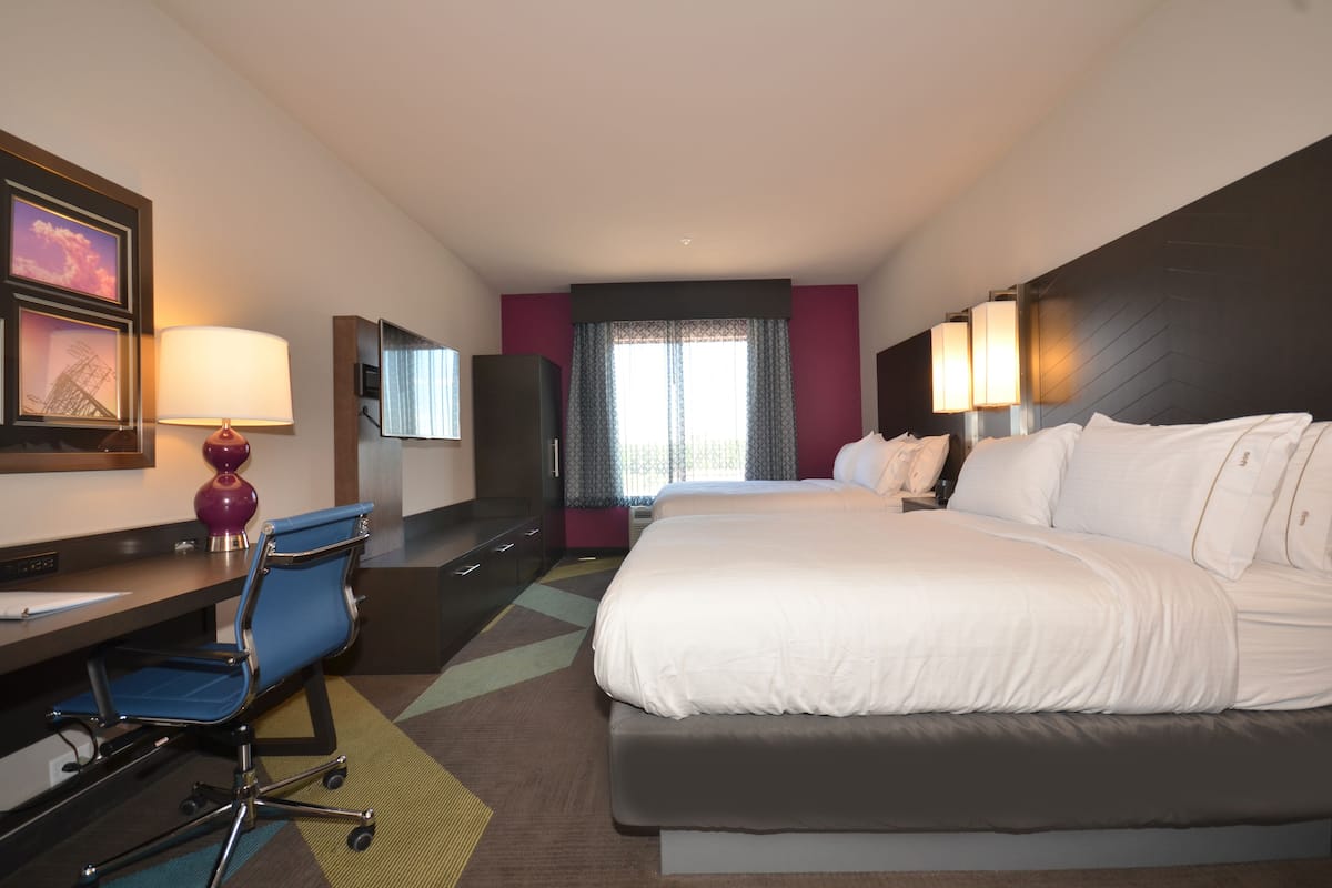 A hotel room with a large bed, a desk with a chair, a TV, and a window with curtains.
