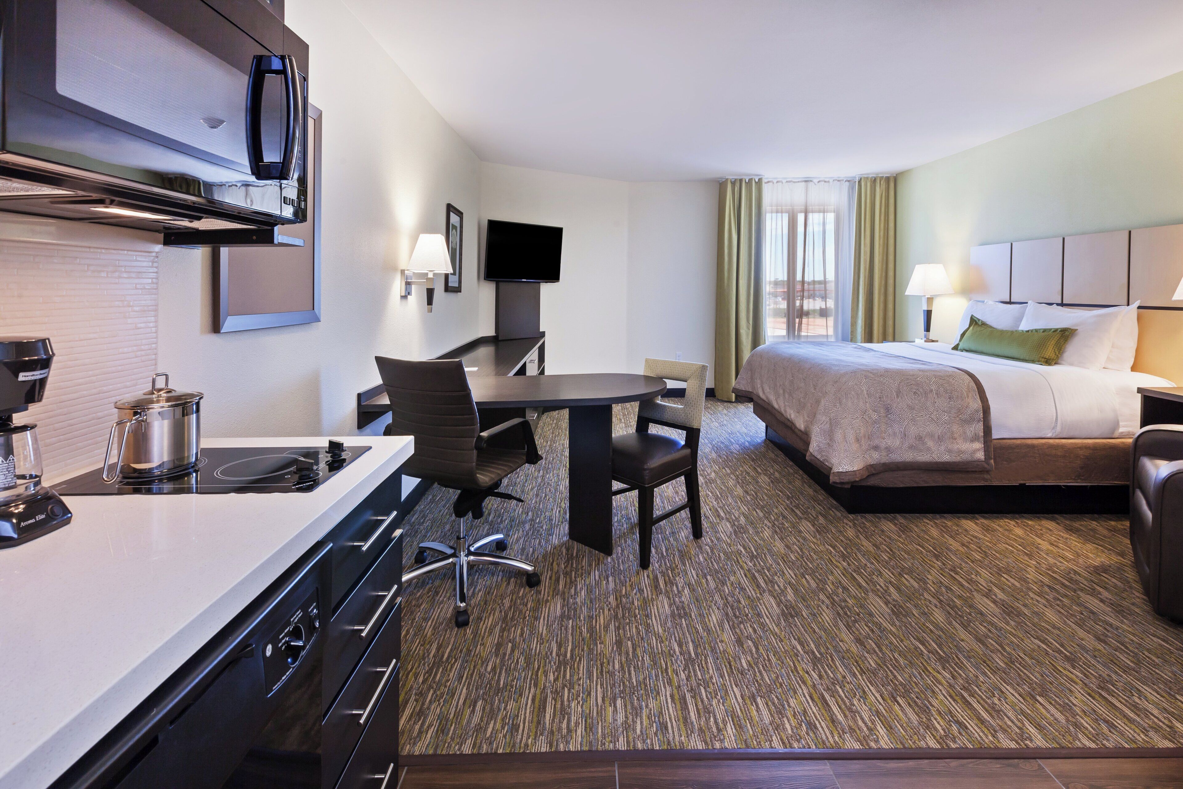A hotel room with a kitchenette, a bed, a desk, and a TV.