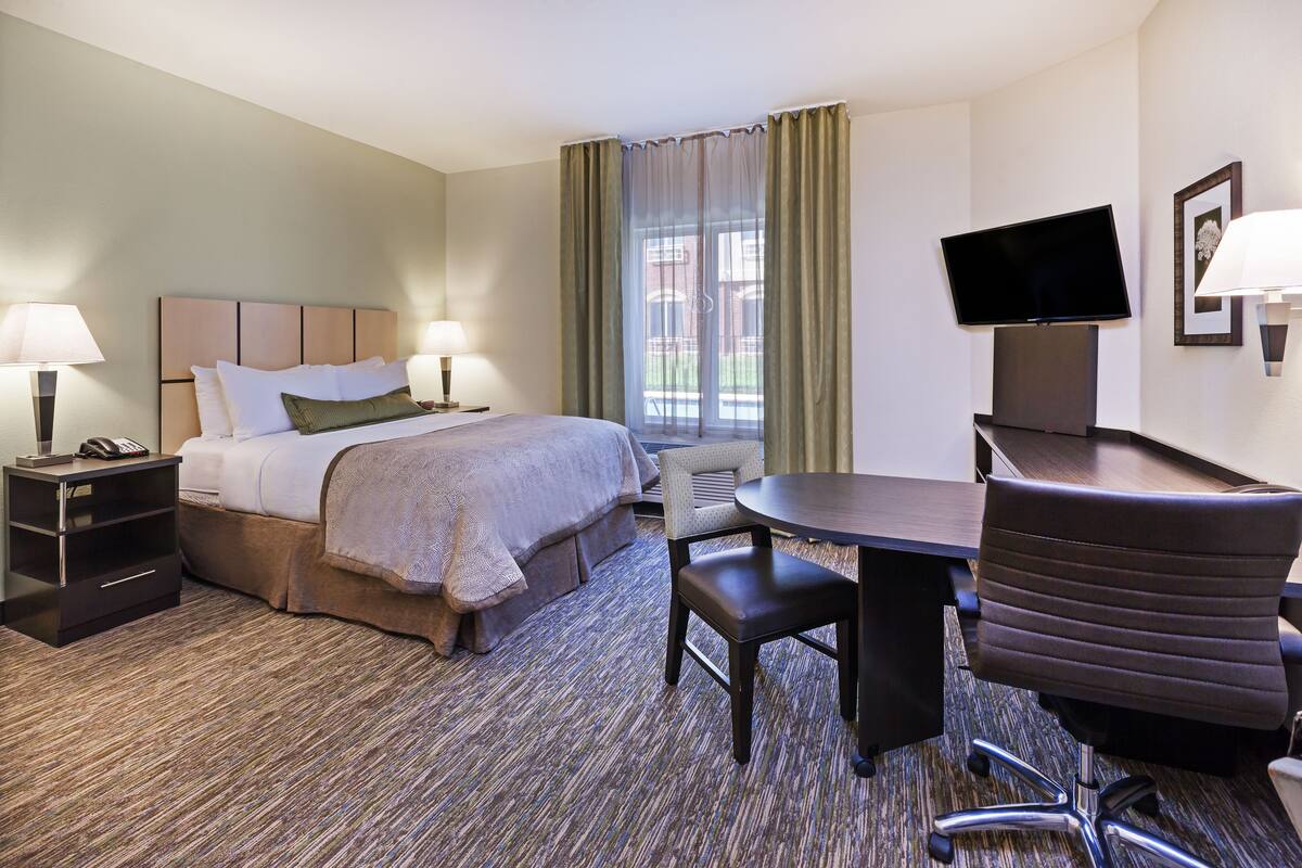 Een hotelkamer met een bed, nachtkastjes, een bureau met stoel, een televisie en een raam met gordijnen.