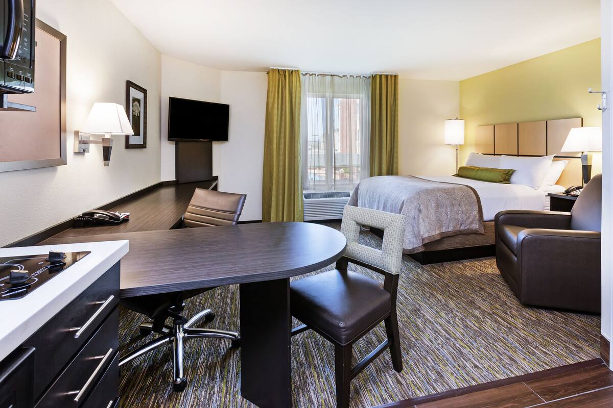 Hotelkamer met een bed, bureau met stoel, bank, televisie en raam met gordijnen.
