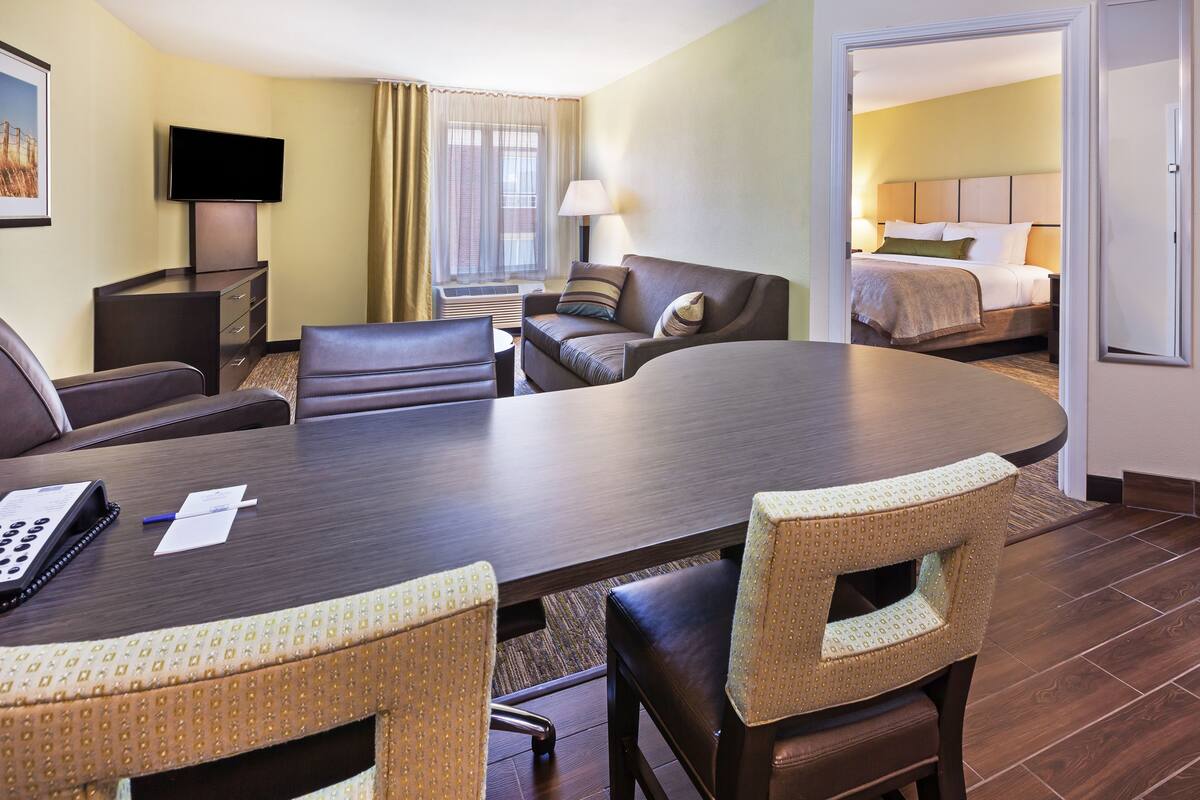 Een hotelkamer met een vergadertafel, vier stoelen, een televisie, een bed en een nachtkastje.