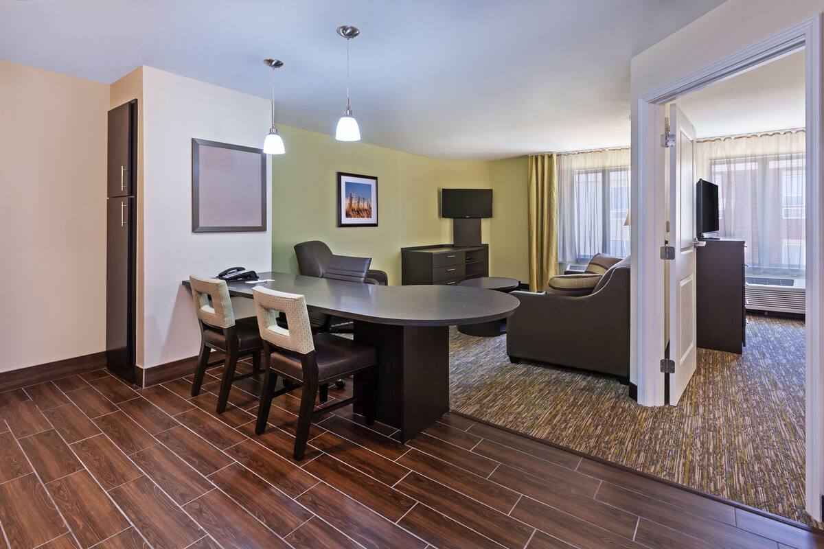 Een hotelkamer met een eethoek, een bank, een televisie en een deur naar een andere kamer.
