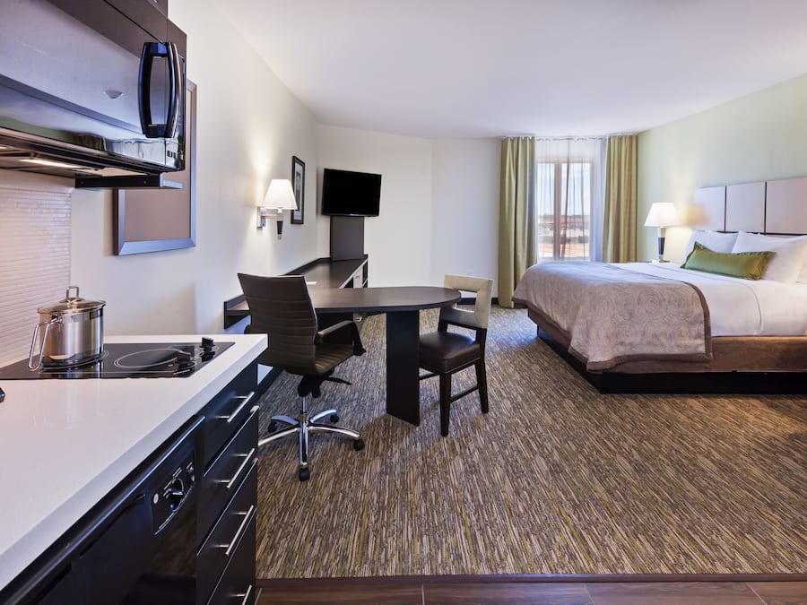 Ein Hotelzimmer mit Küchenzeile, einem Bett, einem Schreibtisch und einem Fernseher.