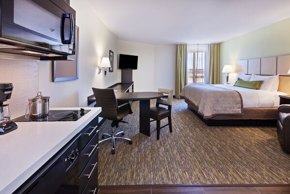 Een hotelkamer met een kitchenette, een bed, een bureau en een televisie.