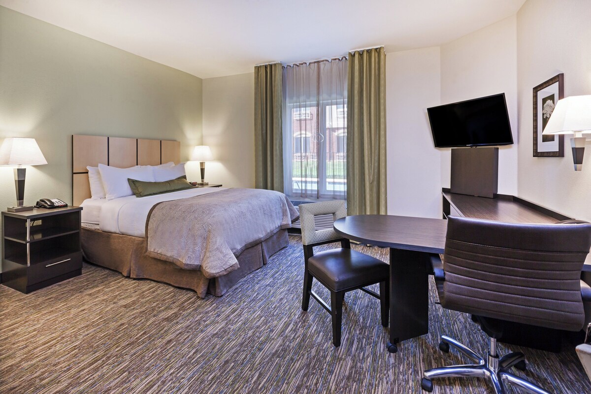 Een hotelkamer met een bed, nachtkastjes, een bureau, een stoel, een televisie en een raam met gordijnen.