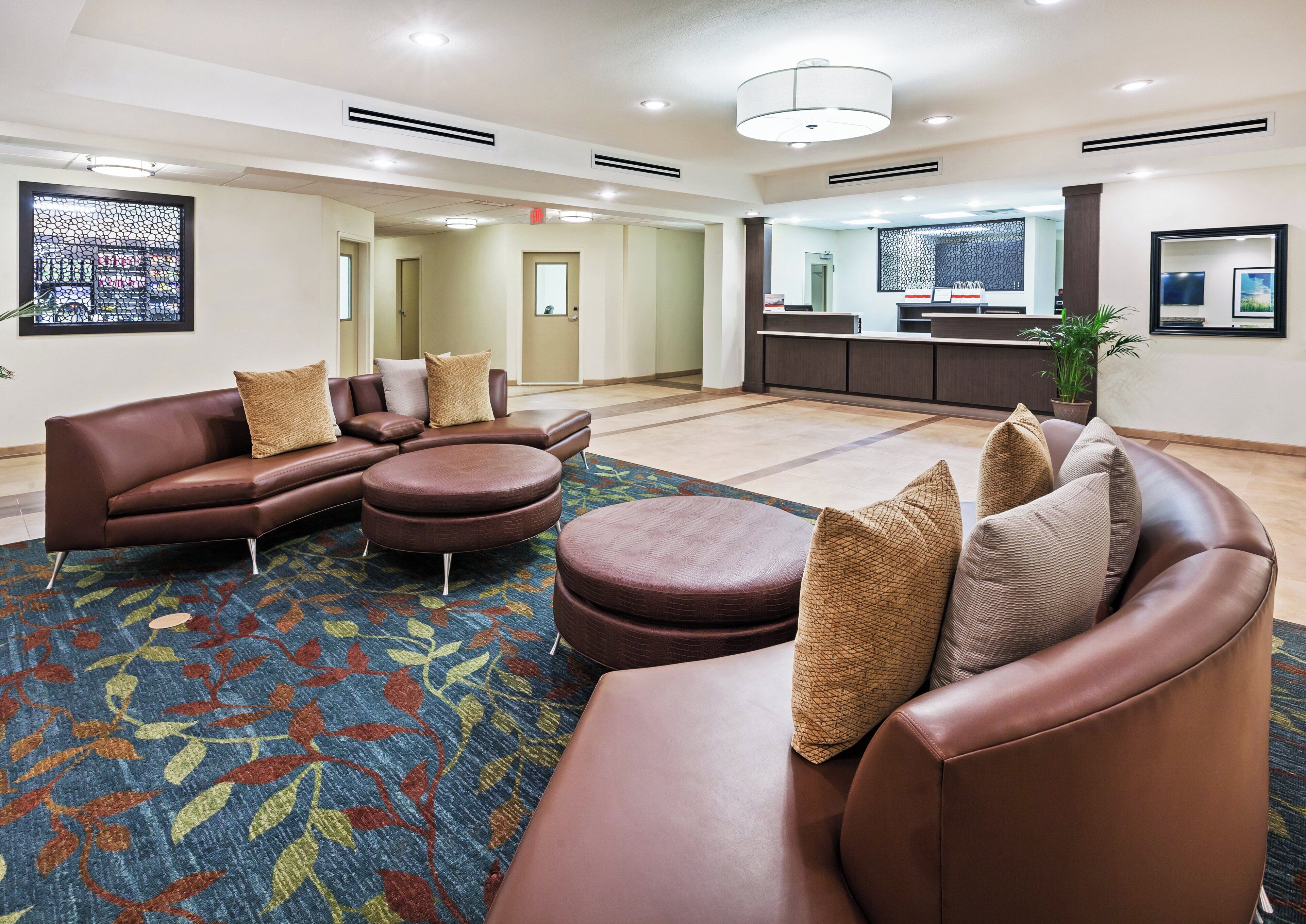 A modern hotel lobby with leather sofas, a patterned rug, and a reception desk.