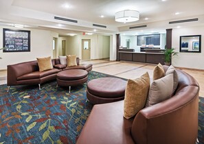 A modern hotel lobby with leather sofas, a patterned rug, and a reception desk.