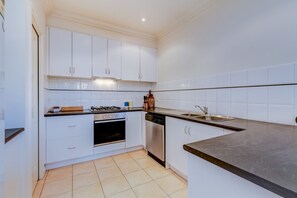 Uma cozinha moderna com armários brancos, fogão, lava-louças e pia.