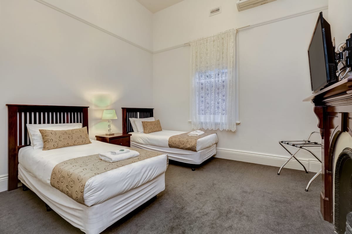 A hotel room with two beds, a TV, a lamp, and a window with curtains.