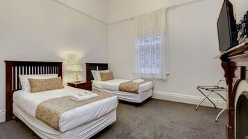 A hotel room with two beds, a TV, a lamp, and a window with curtains.