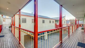 A covered outdoor area with a wooden deck, red railings, and a view of adjacent buildings.