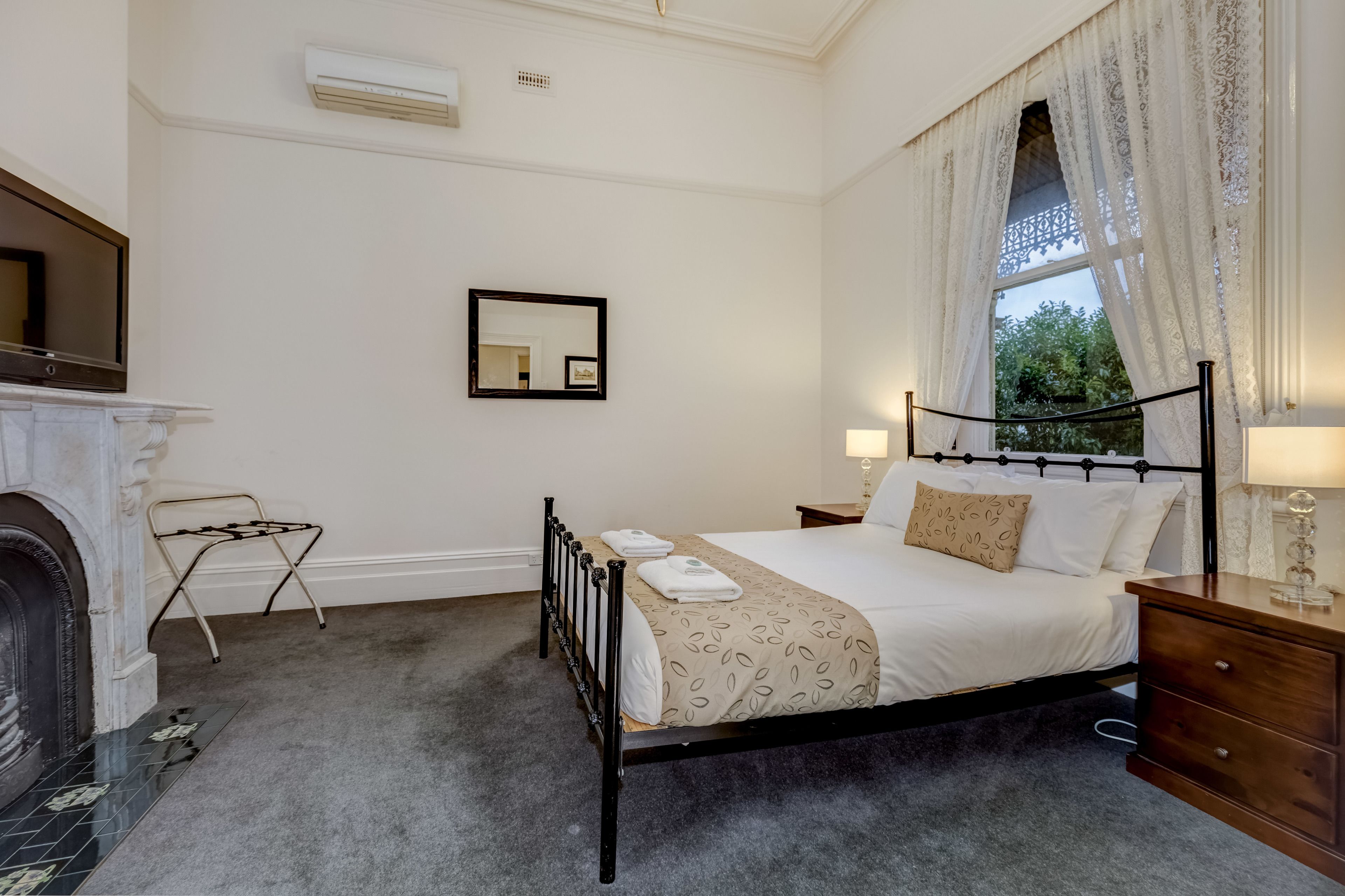 Une chambre à coucher bien rangée, avec un lit, des tables de chevet, un miroir et une cheminée.