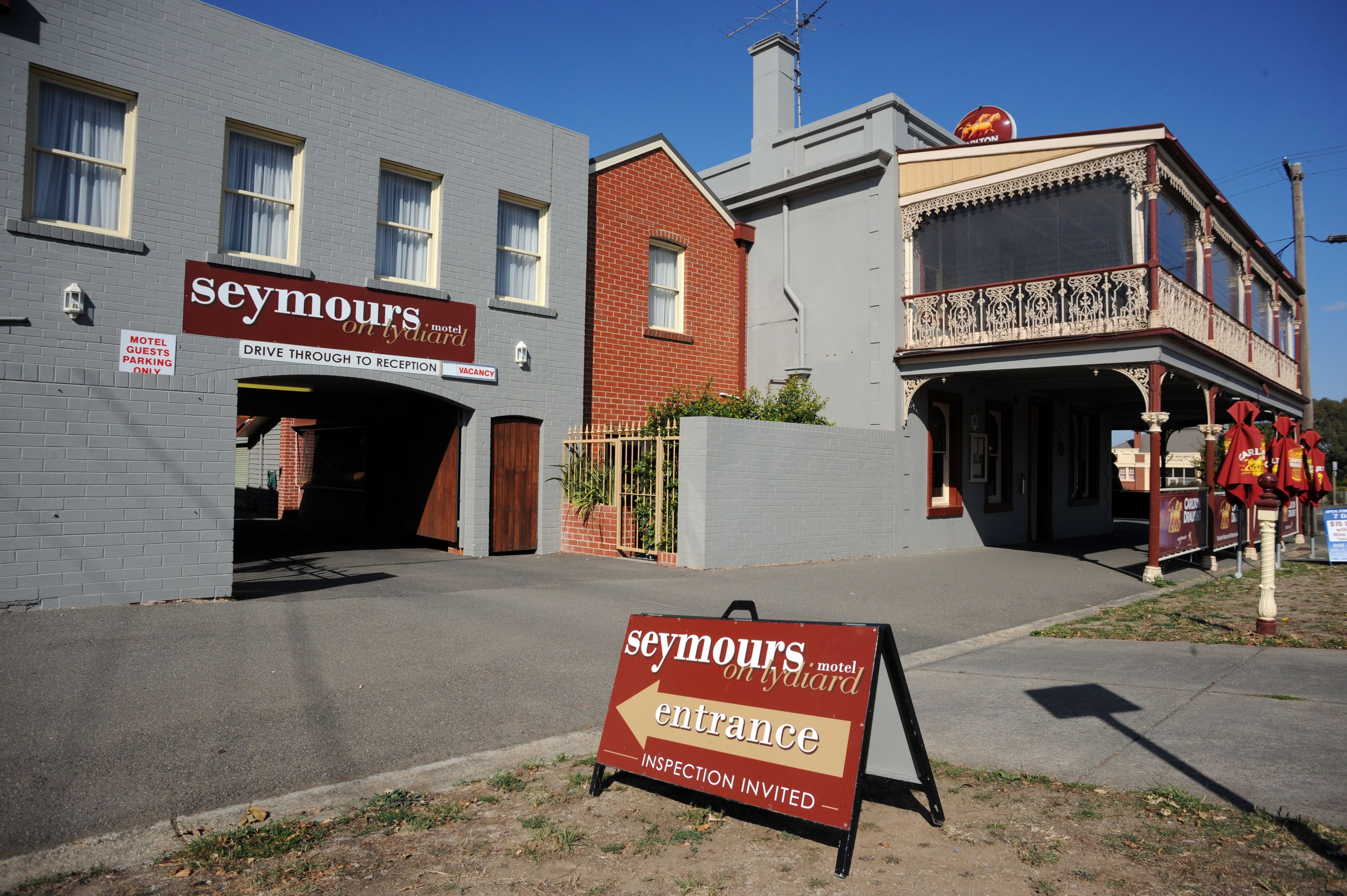 Un motel llamado 'Seymour's on Lydiard' con un letrero que indica 'Acceso directo a la recepción' y 'Inspección bienvenida'.