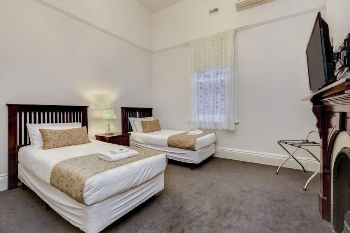 A hotel room with two beds, a television, a small table, and a window with curtains.