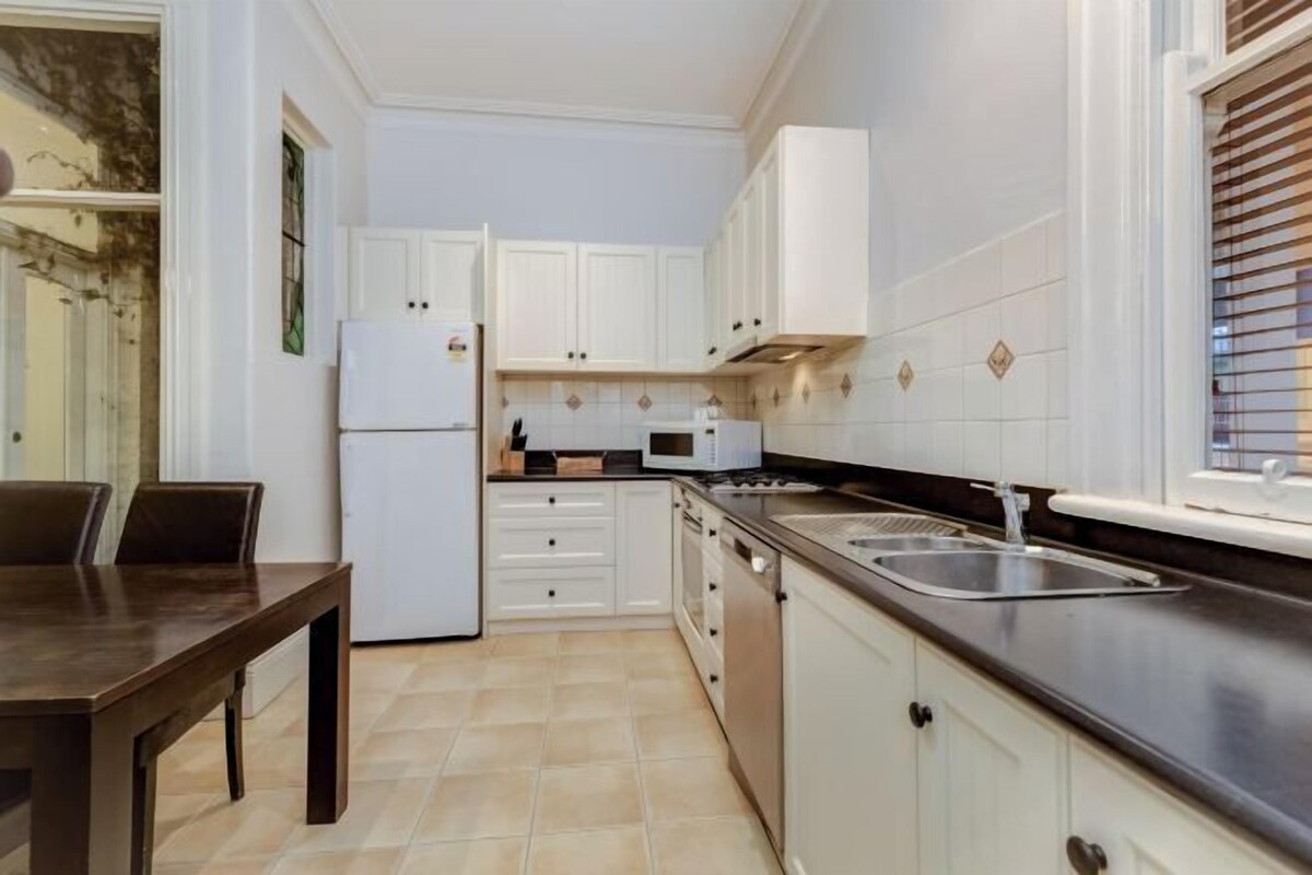 A modern kitchen with white cabinets, a black countertop, and a stainless steel sink.