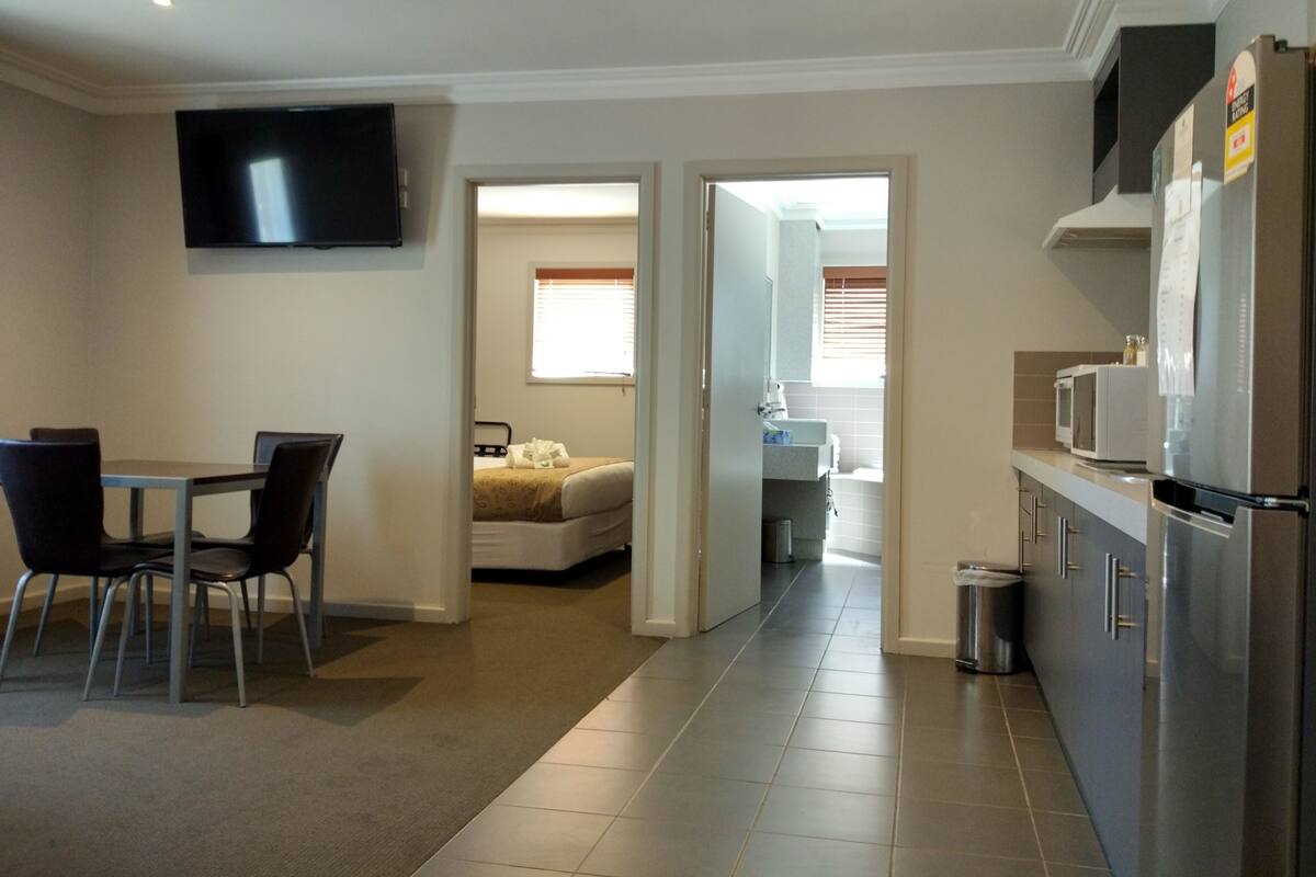 A compact hotel room with a dining area, a bed, and a kitchenette.