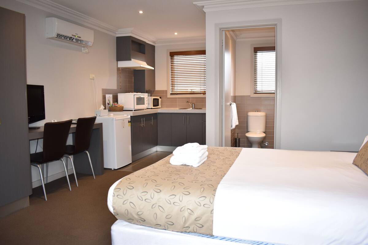 A hotel room with a bed, a desk with a chair, a microwave, a sink, and a toilet.