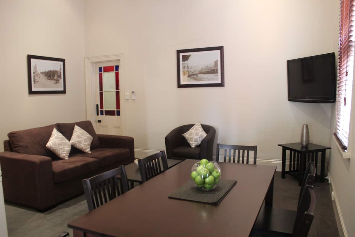 A dining area with a brown table, chairs, a bowl of green apples, and two framed pictures on the wall.