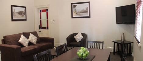 A dining area with a brown table, chairs, a bowl of green apples, and two framed pictures on the wall.