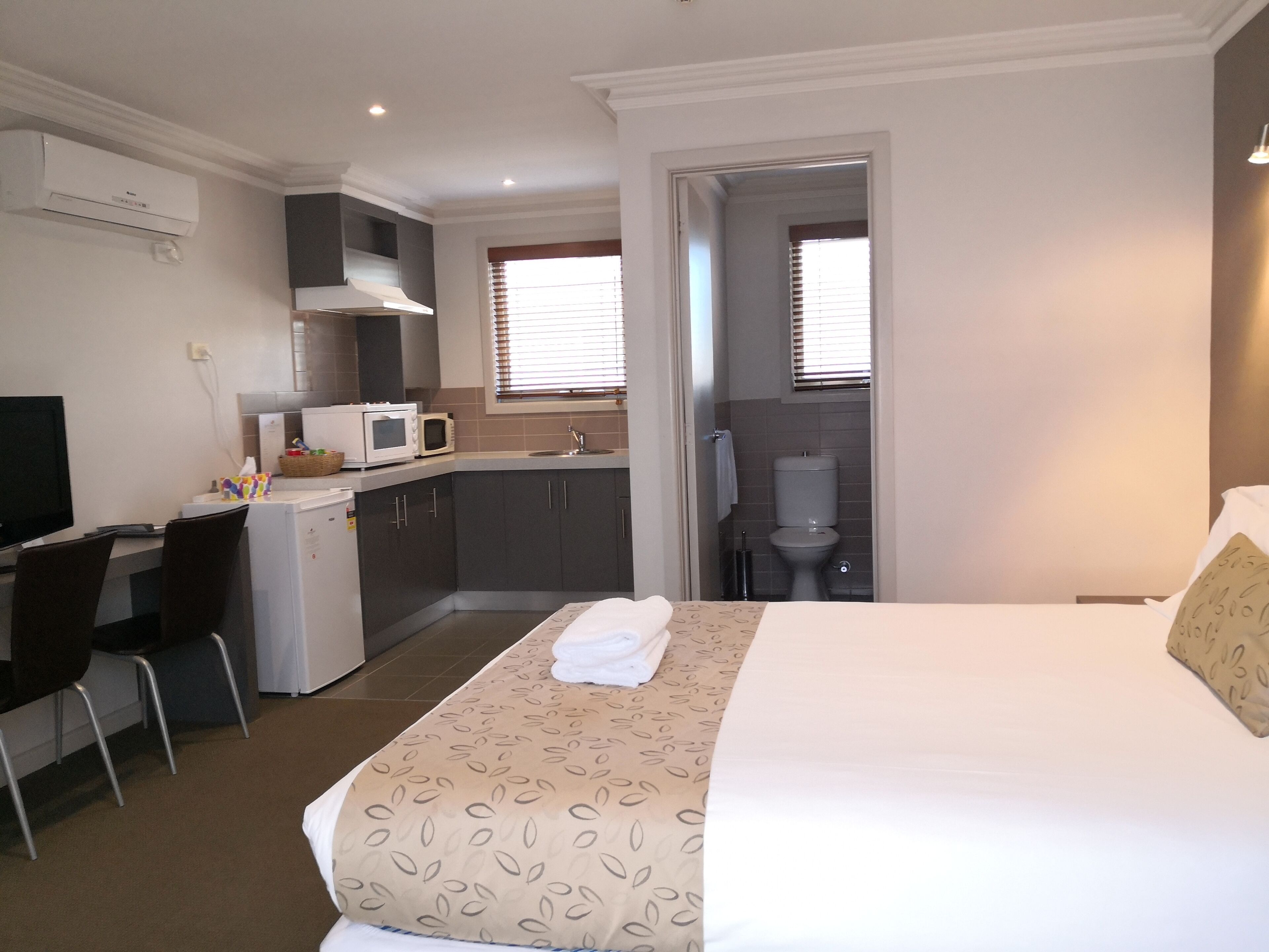 A hotel room with a bed, a desk with a computer, a kitchenette, and a bathroom.
