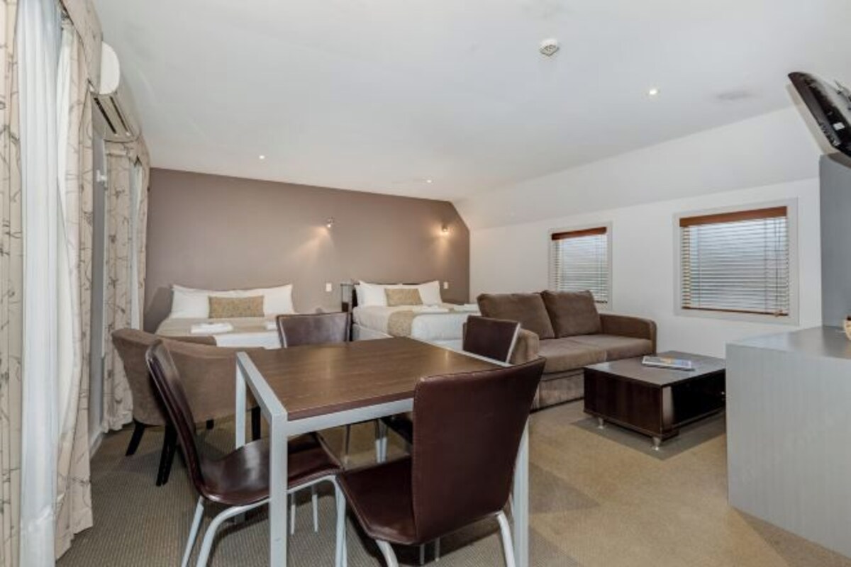 A modern hotel room with a dining area, a sofa set, a coffee table, and a TV.