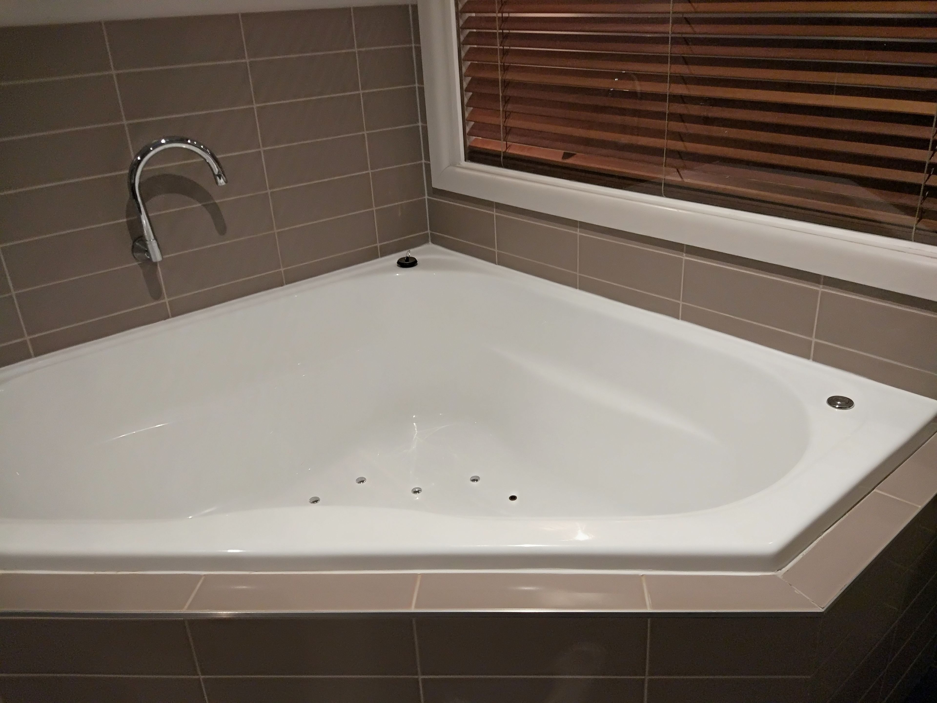 Un baño moderno con una bañera independiente, un cabezal de ducha manual y una ventana con persianas.