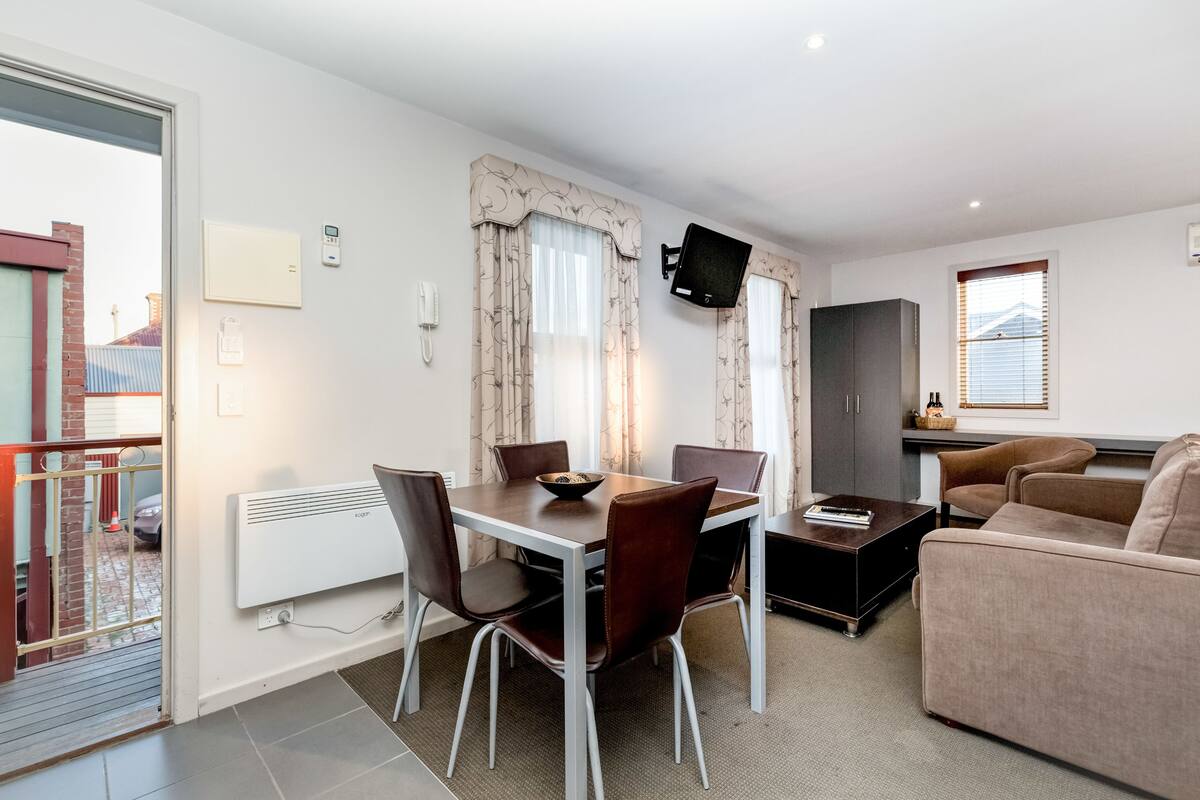 A modern living room with a dining area, a flat-screen TV mounted on the wall, and a sofa.