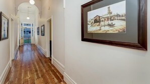 A hallway with wooden flooring, white walls, and framed pictures on the walls. - Seymours on Lydiard (Soldiers Hill)