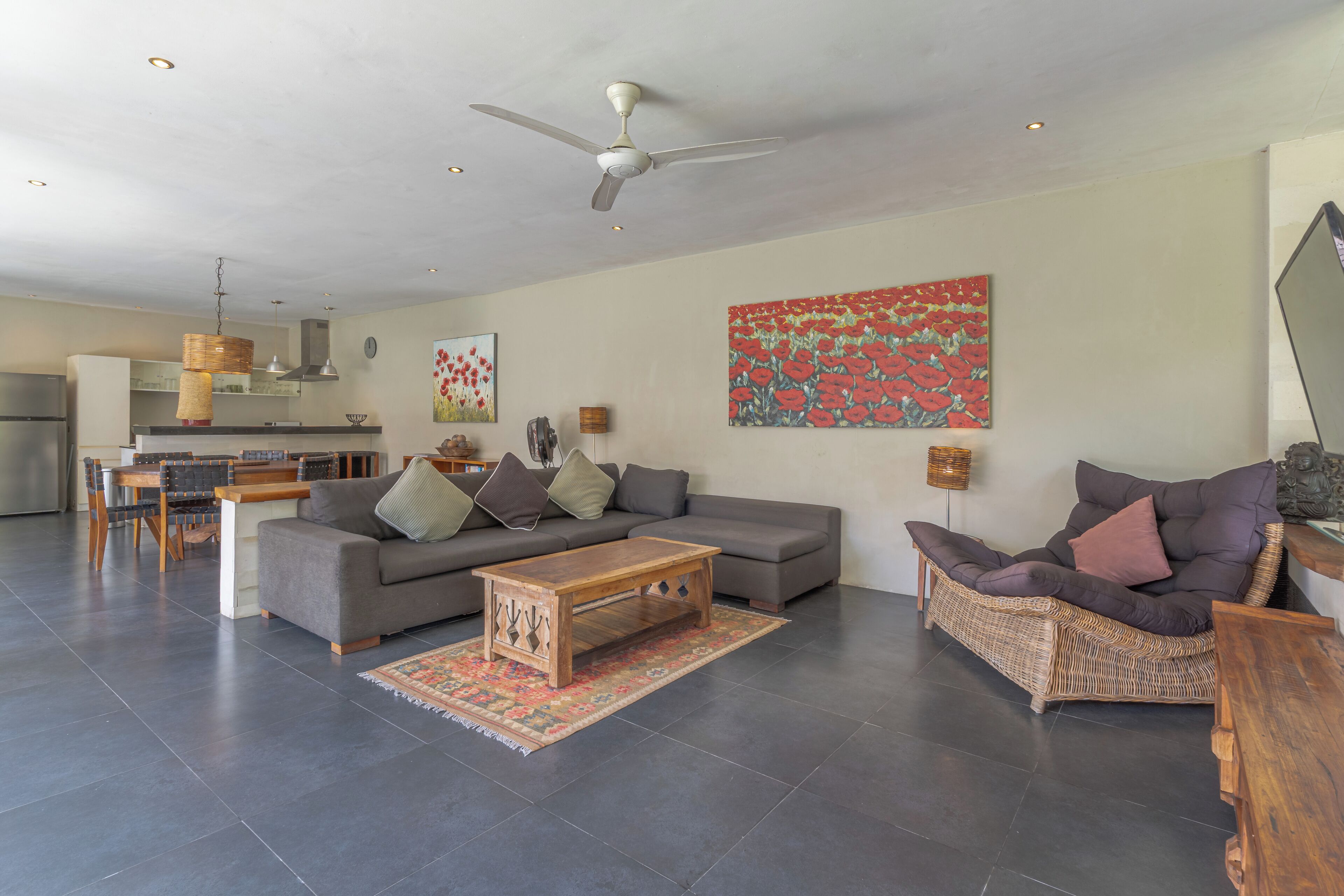 Una sala moderna con un sofá, una mesa de centro y una silla de mimbre. Hay una zona de comedor con una mesa y sillas, y una cocina al fondo.